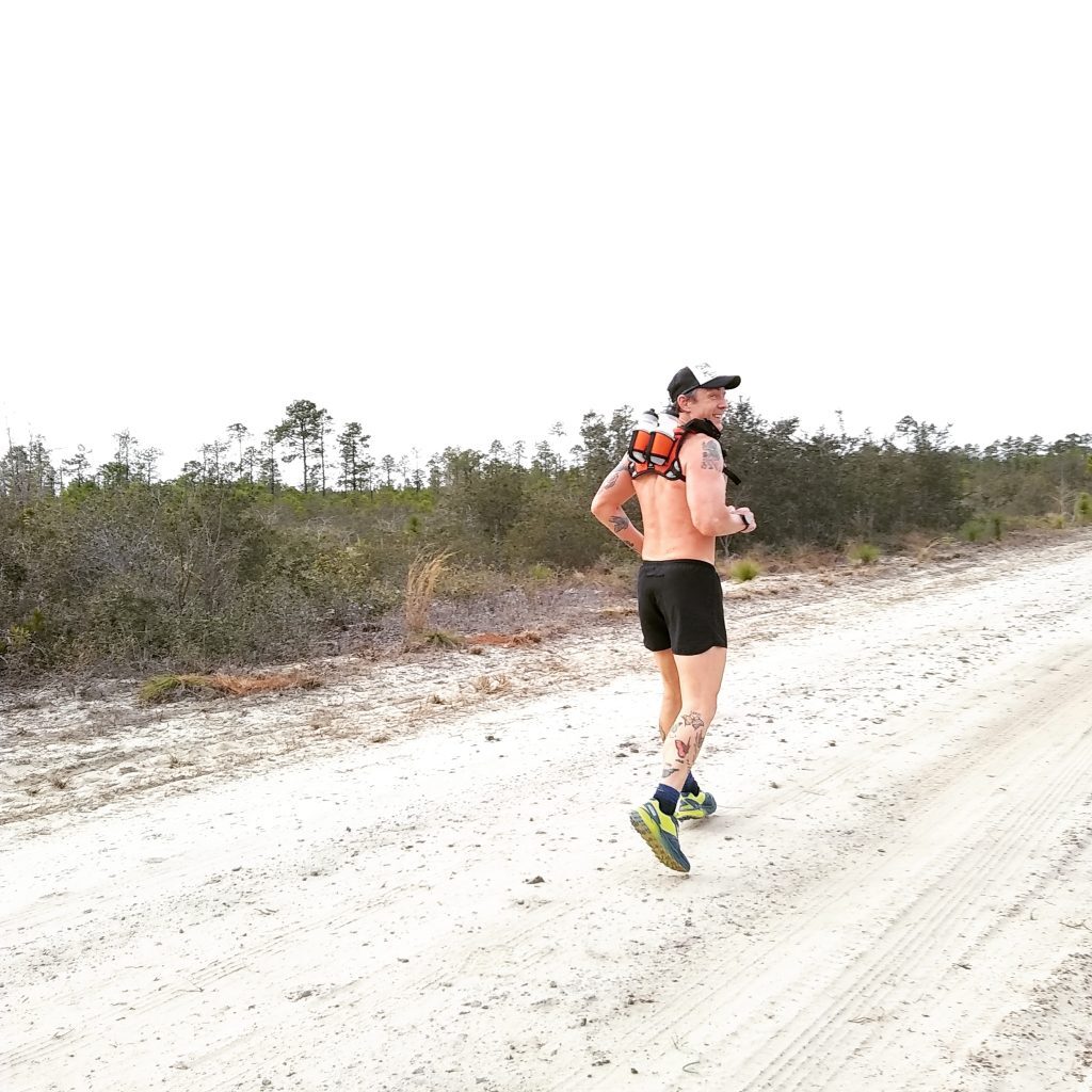Trail runner running down a sandy, dirt road in the summer