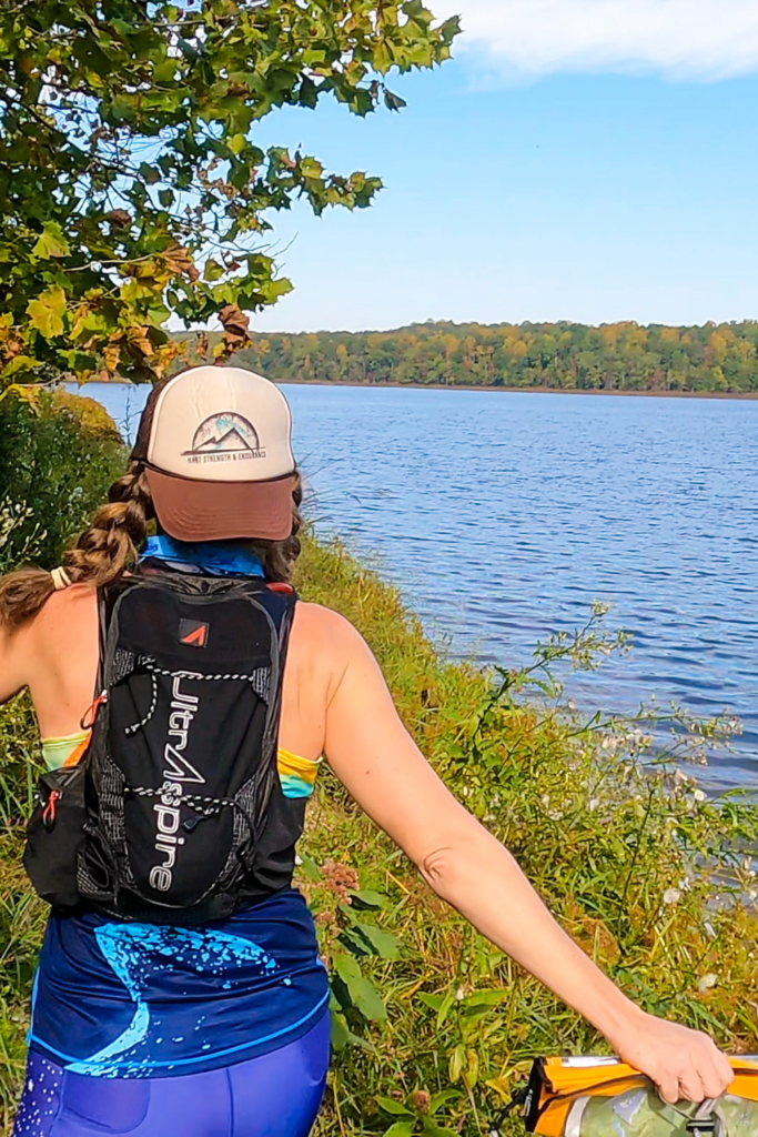 Heather Hart usando o pacote de hidratação UltrAspire Zygos 5.0 enquanto corre ao lado de um lago durante uma corrida de aventura