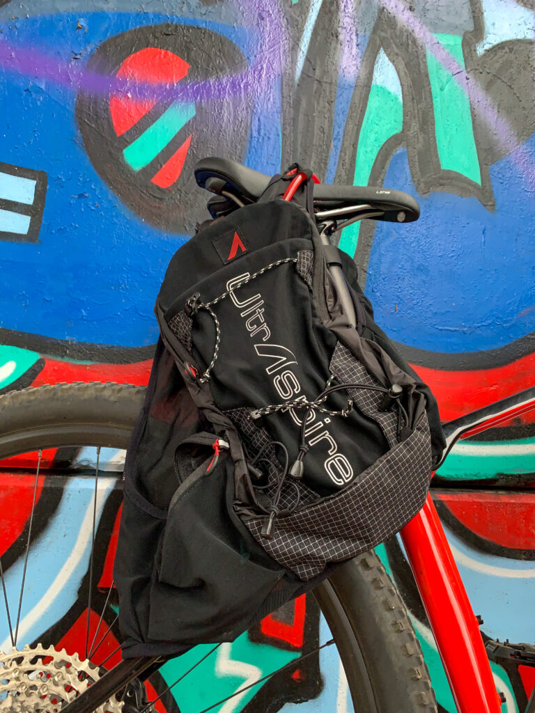 UltrAspire Zygos 5.0 pendurado em um assento de bicicleta em frente a uma parede coberta de grafite