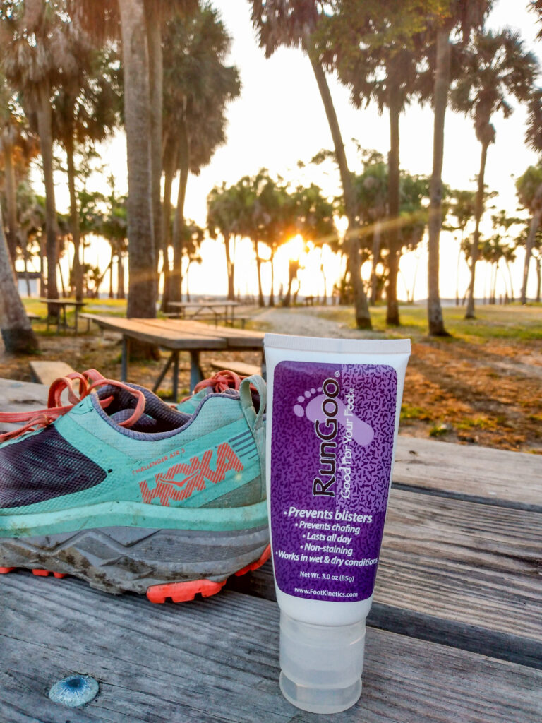 Run Goo foot lube to prevent blisters sitting on a picnic table next to a running shoe in the sunrise