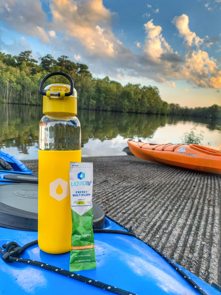 Liquid IV Energy Multiplier leaning on a water bottle next to kayaks at a boat launch