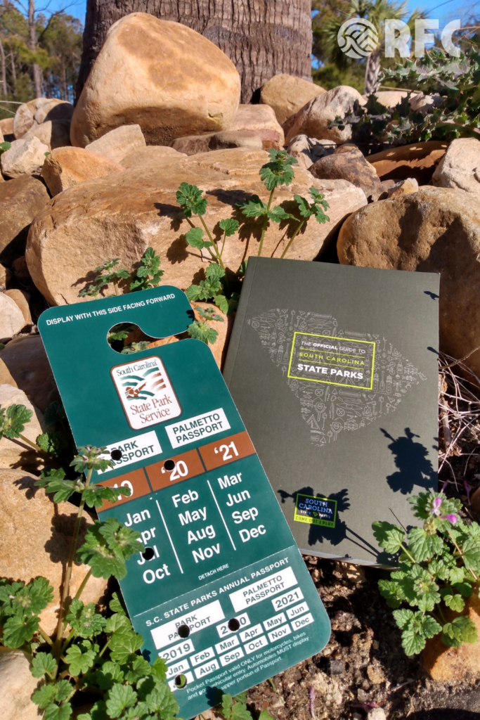 Image of a South Carolina State Park Pass and a South Carolina State Parks Guide on rocks in the outdoors
