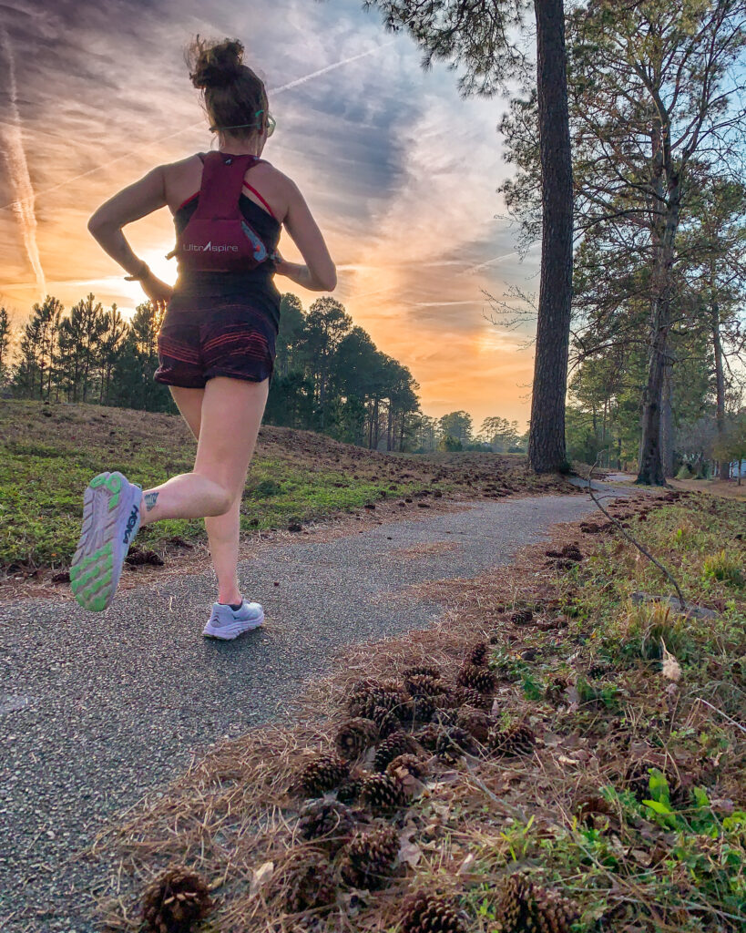 Heather Hart running on a paved path at sunset wearing the UltrAspire Basham Race Vest