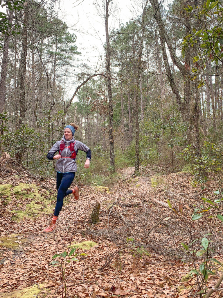 trail runner runs on a leaf covered trail in the forest