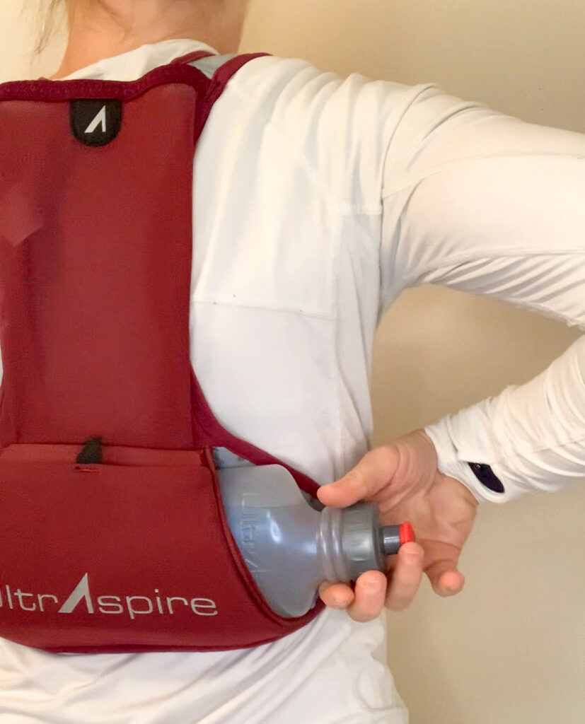 rear view of an athlete reaching for the bottle of the UltrAspire Basham Race Vest