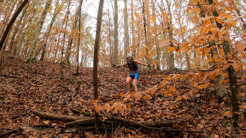 Woman running down a steep leaf covered hill in the fall