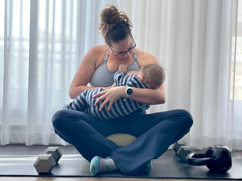 Maggie Seymour breastfeeding her child while surrounded by various dumbbells and kettlebells