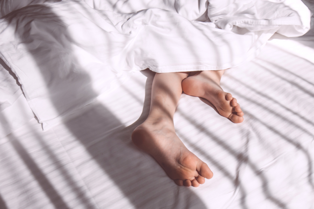 Why Does Plantar Fasciitis Hurt More in the Morning? Image of a persons feet sticking out from under blankets in a bed