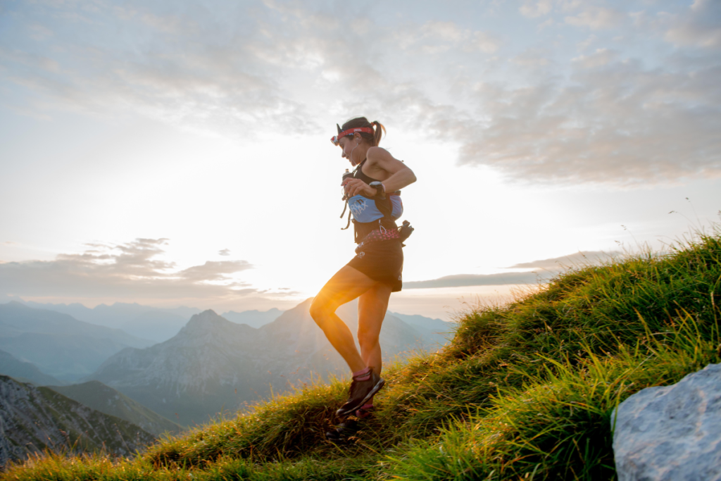 Woman runs down a mountain top at sunrise wearing a headlamp and hydration vest