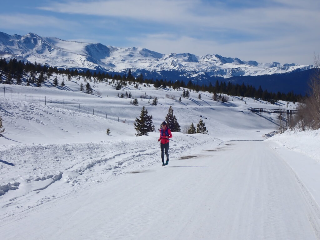 Woman on a winter trail run with snow on the ground and mountains in the background