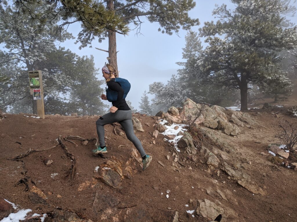 Lexi Miller running up a dirt and snow covered ridge during a winter trail run