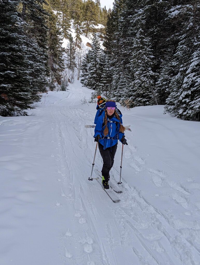 Lexi Miller ski touring down a trail with her toddler son in a pack on her back